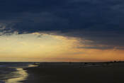 Photo of a beach at sunset, with dark purple clouds hanging ominously above